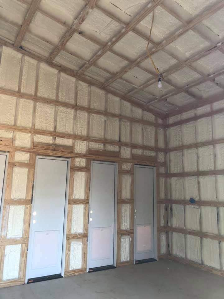 Interior view of a workshop or garage under construction, with spray-foam insulated walls and ceiling and three white doors.