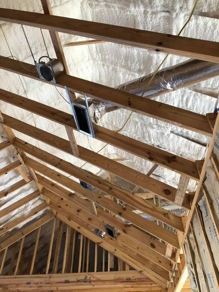 Unfinished attic interior featuring wooden ceiling joists, spray foam insulation, and HVAC ductwork with recessed lighting.