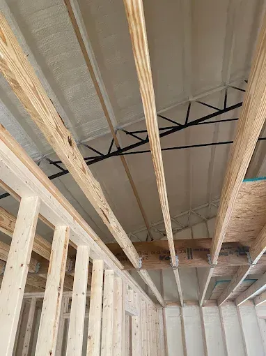 Interior view of wooden wall studs and ceiling joists in a building under construction, with a black metal roof truss.