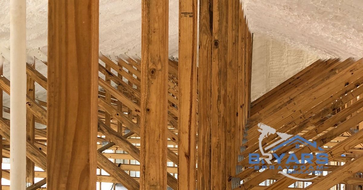 Interior view of unfinished wooden roof trusses and spray foam insulation in an attic space.