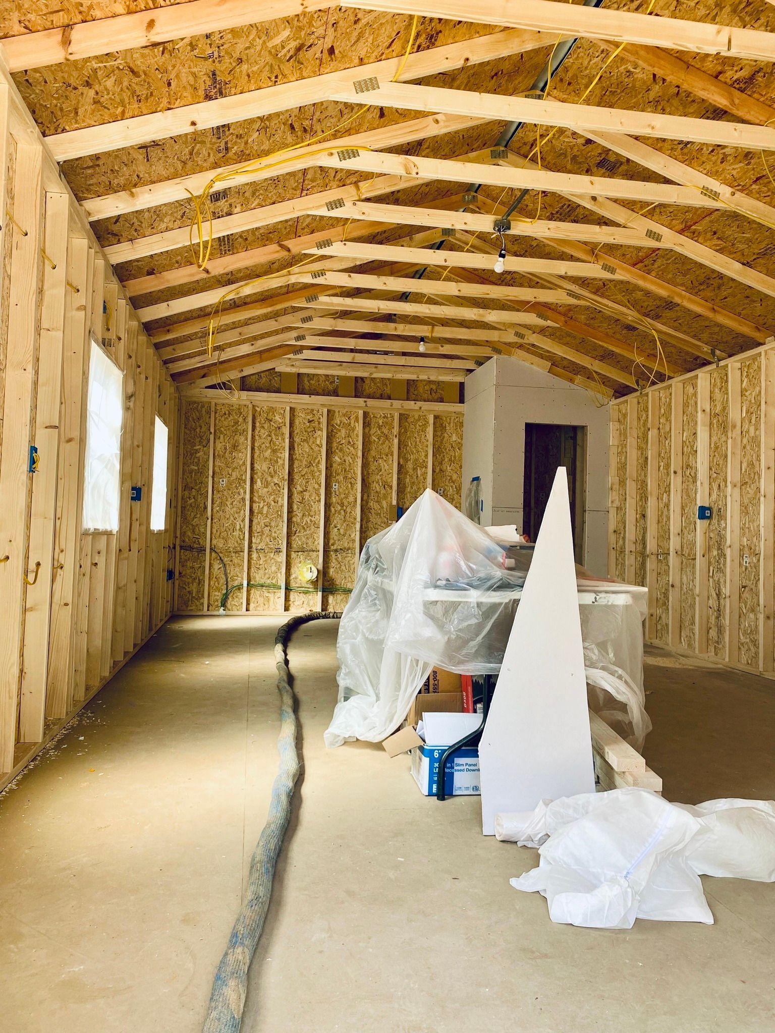 Interior of an unfinished wooden shed with exposed wall studs, rafters, and debris on the concrete floor.