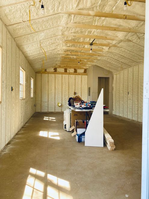 Interior view of a workshop or shed with cream-colored spray foam insulation on the walls and ceiling and a concrete floor.