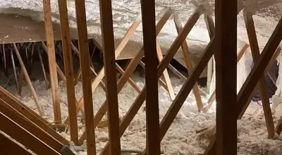 A view through wooden wall studs at a snowy attic floor covered in loose-fill insulation.