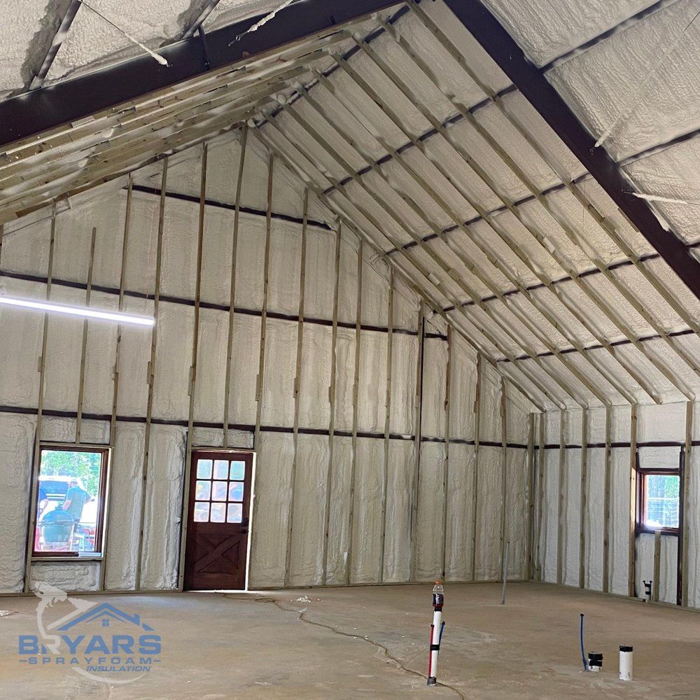 Interior of a metal building under construction with white spray foam insulation on the walls and ceiling.