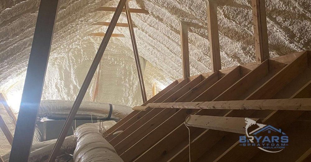 An attic interior with wooden rafters and ductwork, featuring roof decking insulated with white spray foam.