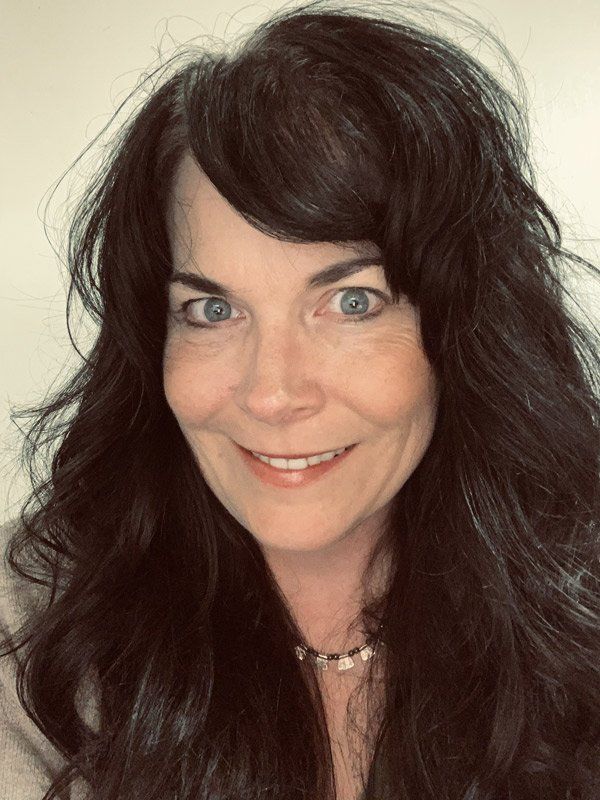 A woman with long dark hair and blue eyes is smiling for the camera.