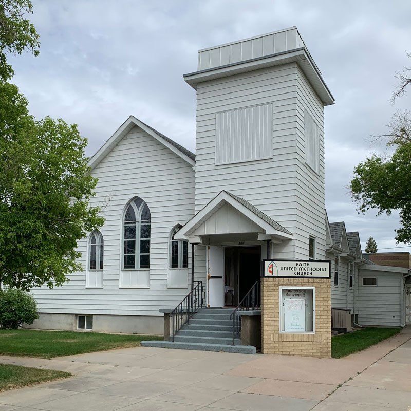 A white church with a sign that says Faith United Methodist Church on it