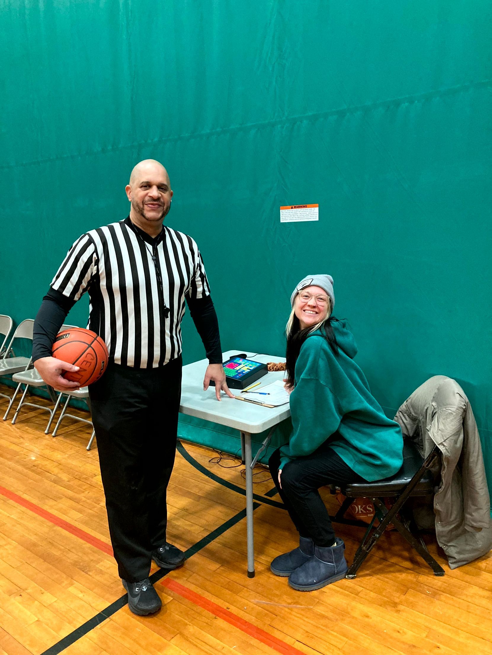 Basketball game: Referee handing ball to smiling player as opponent looks on.