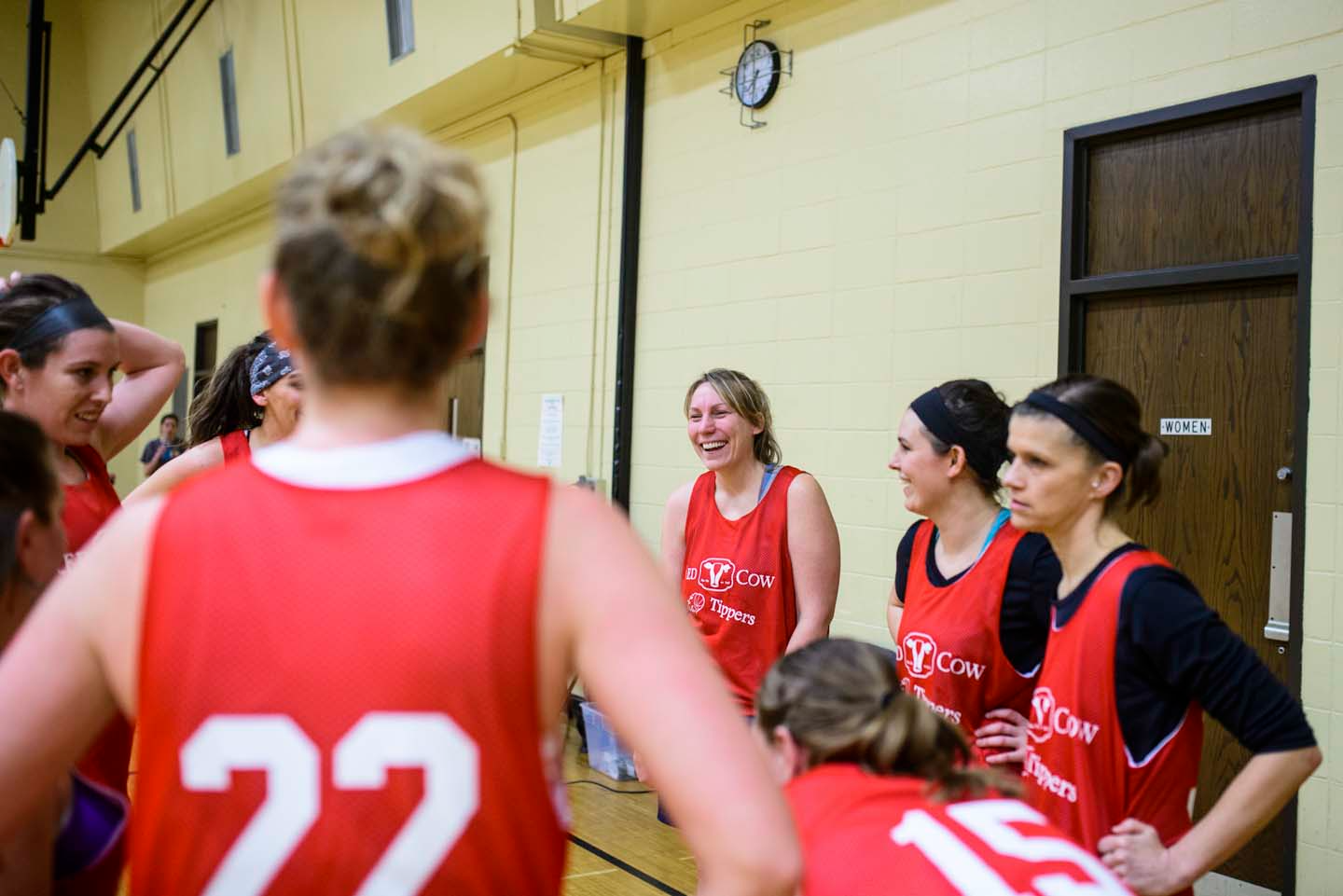 Basketball players in red jerseys huddle, smiling and strategizing in a gym.
