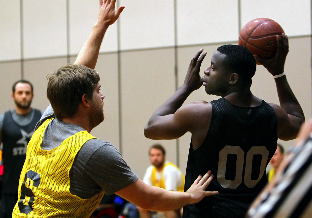 Basketball player holding ball, defended by a player with raised arms in indoor court setting.