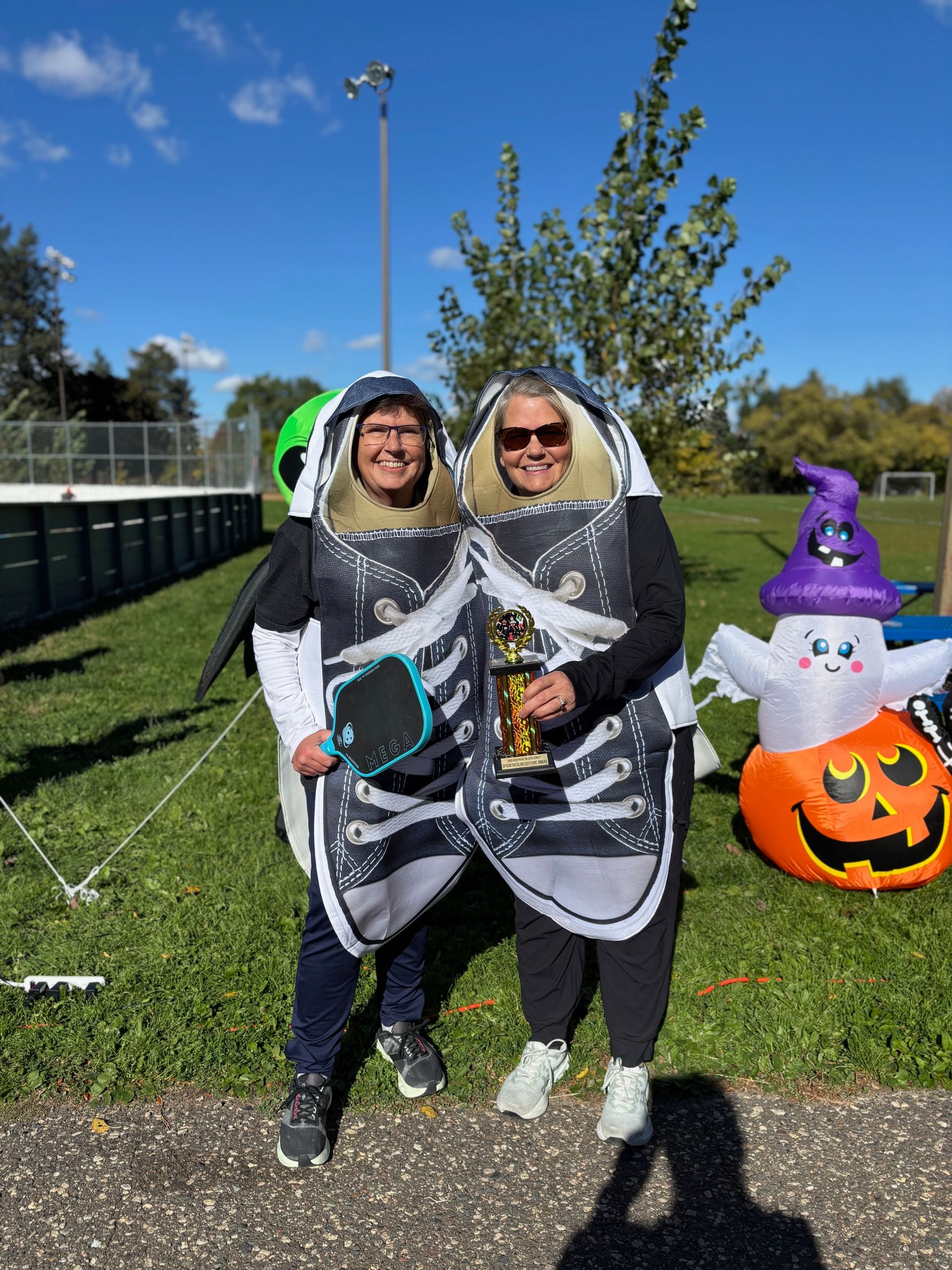 Two people in shark costumes posing outdoors beside a Halloween inflatable snowman and pumpkin.