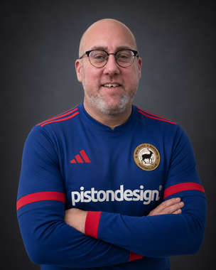Man in blue sports jersey with arms crossed, smiling against a dark background.