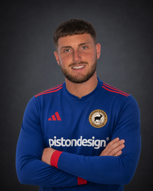 Soccer player in blue jersey with arms crossed, smiling against a dark background