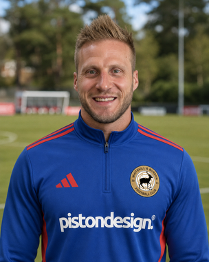 Smiling man in blue sports jacket standing on a soccer field
