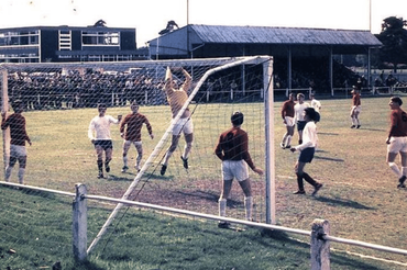 Soccer match in progress near the goal, with players and a crowd in the stands behind them.