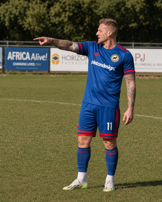 Soccer player in blue kit points left on a grass field during a match
