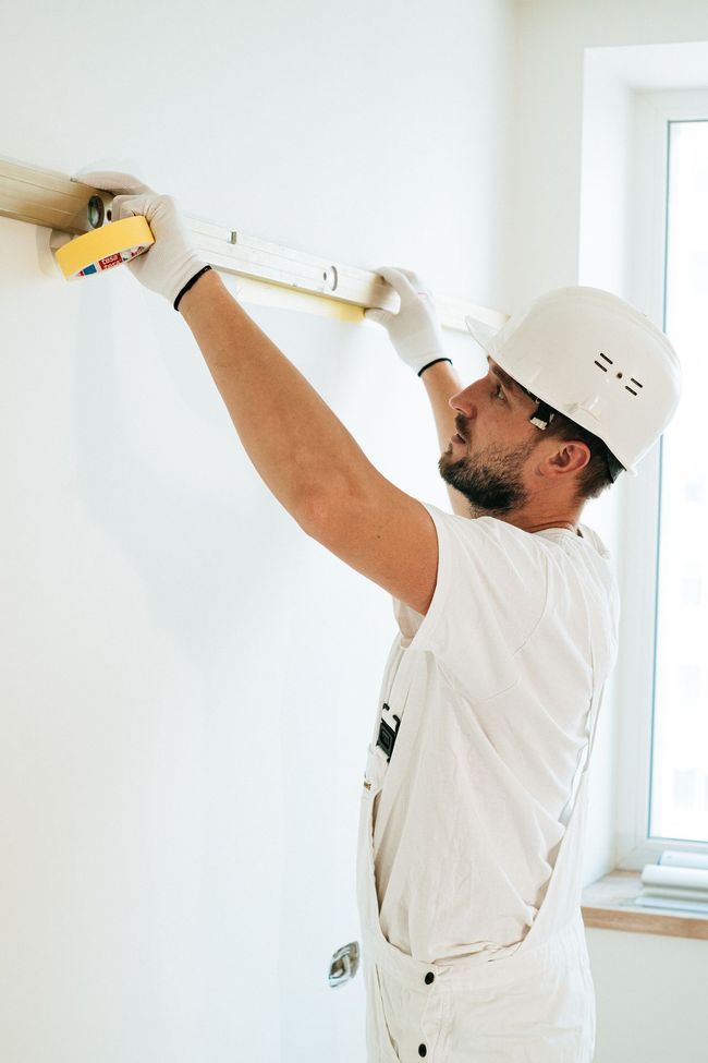 Worker drilling into a white wall near a window in a bright room