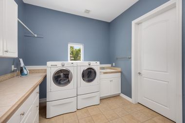 Bright laundry room with blue walls, white washer and dryer, beige counters, and a white door.