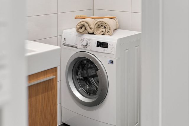 Front-loading washing machine beside a sink, with folded towels on top in a tiled laundry room