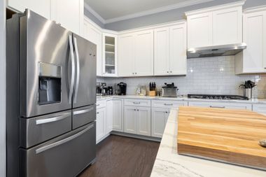 Modern white kitchen with stainless steel refrigerator, tiled backsplash, and butcher-block island countertop