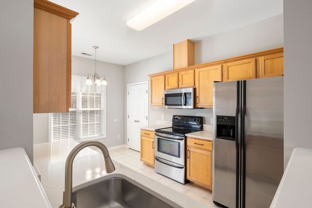 Bright kitchen with stainless steel appliances, wooden cabinets, and a sink in the foreground.