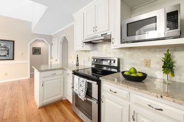 Bright white kitchen with stainless steel appliances, granite counters, and light wood floors