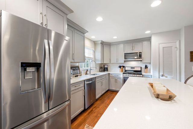 Modern gray kitchen with stainless steel appliances, white island, and warm wood floor