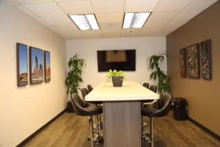 Modern conference room with long table, wall-mounted TV, chairs, plants, and city artwork.