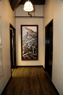 Narrow hallway with dark doors, wood floor, and a framed abstract artwork at the end.
