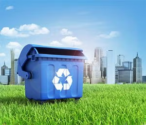 Blue recycling bin with white recycle symbol on green grass in front of a city skyline