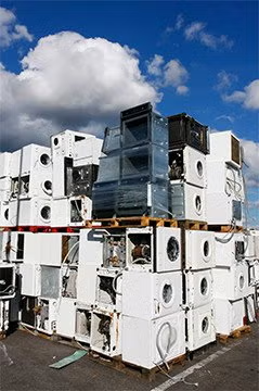Stacked white air-conditioning units in an outdoor scrapyard under a blue sky