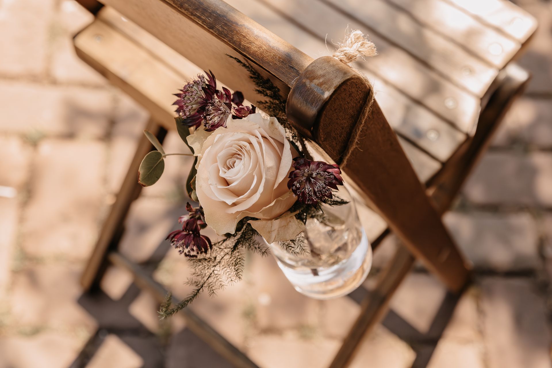 Kleine bloemendecoratie met roos aan een houten stoel, detail van een romantische en persoonlijke huwelijksceremonie.