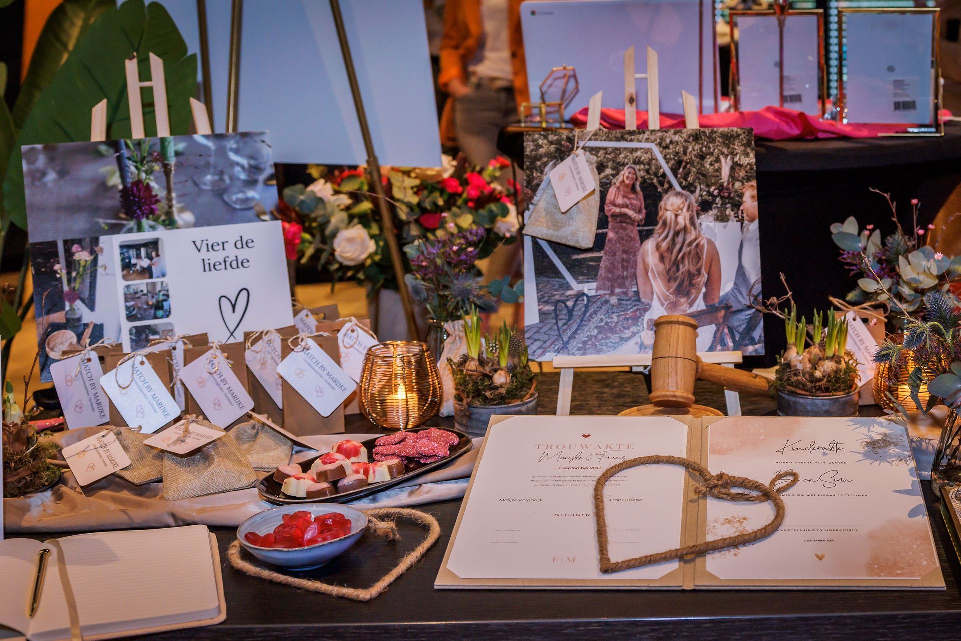 Stylingtafel met liefdevolle details zoals foto’s, kaarsen, trouwboek en hartvormige decoratie, passend bij een persoonlijke huwelijksceremonie.