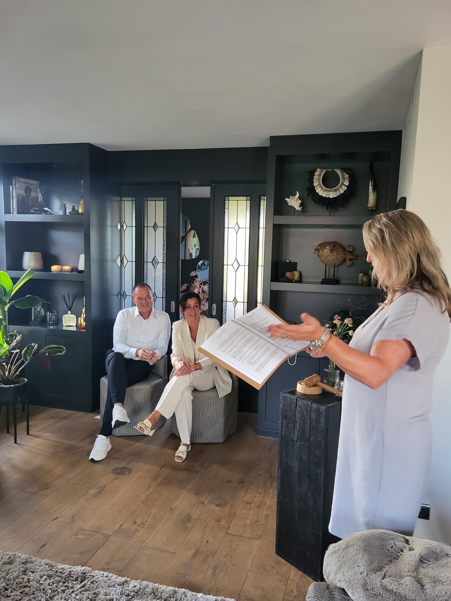Ceremoniespreker Marijke spreekt een bruidspaar toe tijdens een intieme huwelijksceremonie binnenshuis, met persoonlijke aandacht en warmte.
