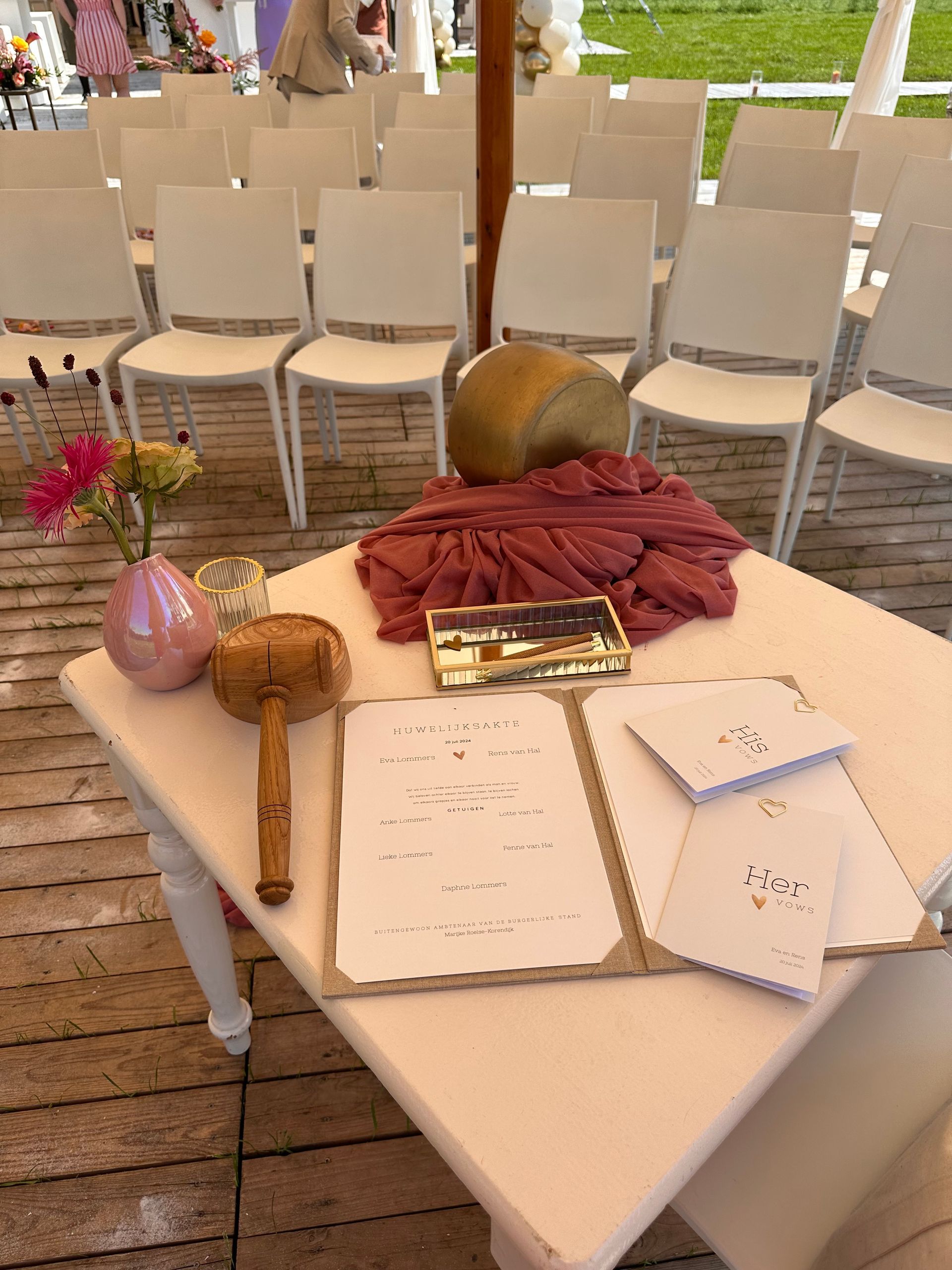 Detail van een trouwceremonie met witte stoelen, decoratieve kussens en accessoires op een tafel, voorbereid voor een persoonlijke buitenbruiloft.