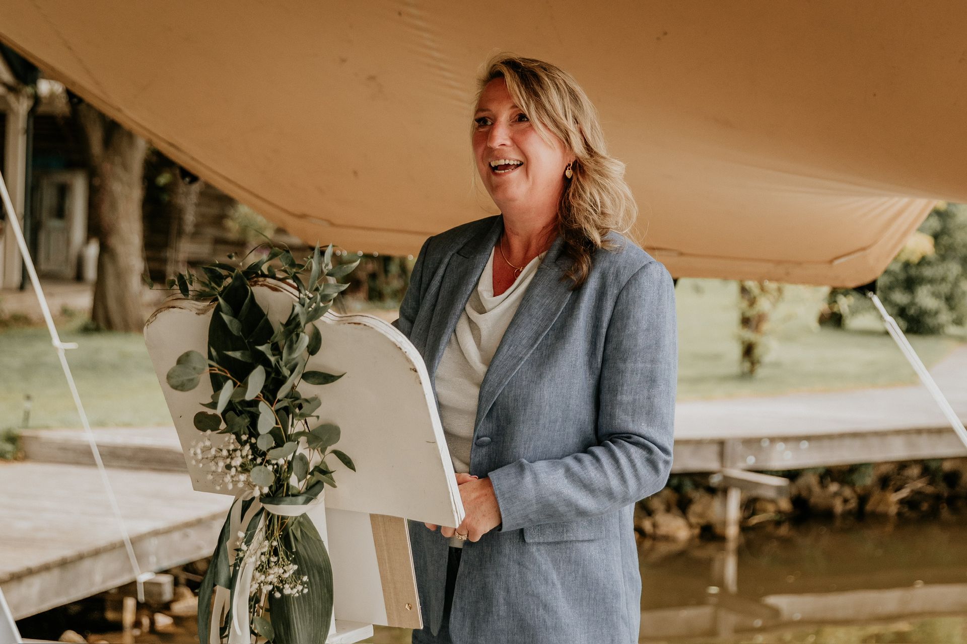 Trouwambtenaar Marijke spreekt tijdens een persoonlijke huwelijksceremonie in de buitenlucht bij het water.