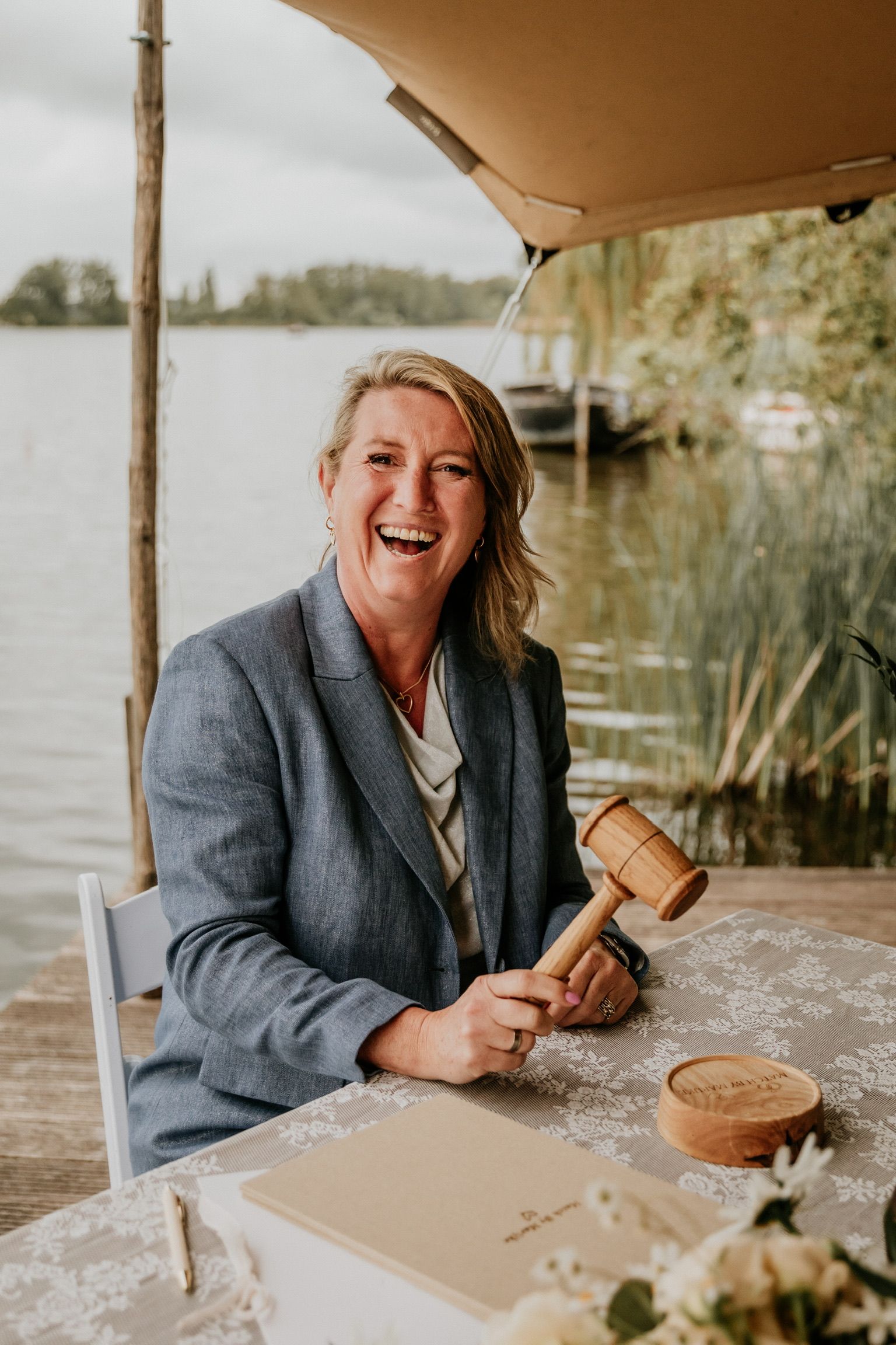 Lachend portret van trouwambtenaar Marijke aan het water, met een open en warme uitstraling tijdens een buitenhuwelijk.
