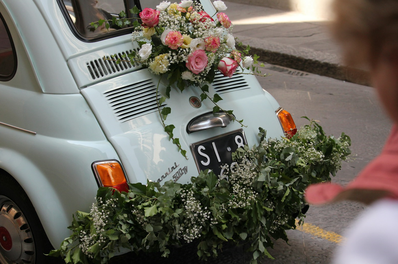 Vintage trouwauto versierd met bloemen en groen, symbool voor een romantische en persoonlijke huwelijksdag.