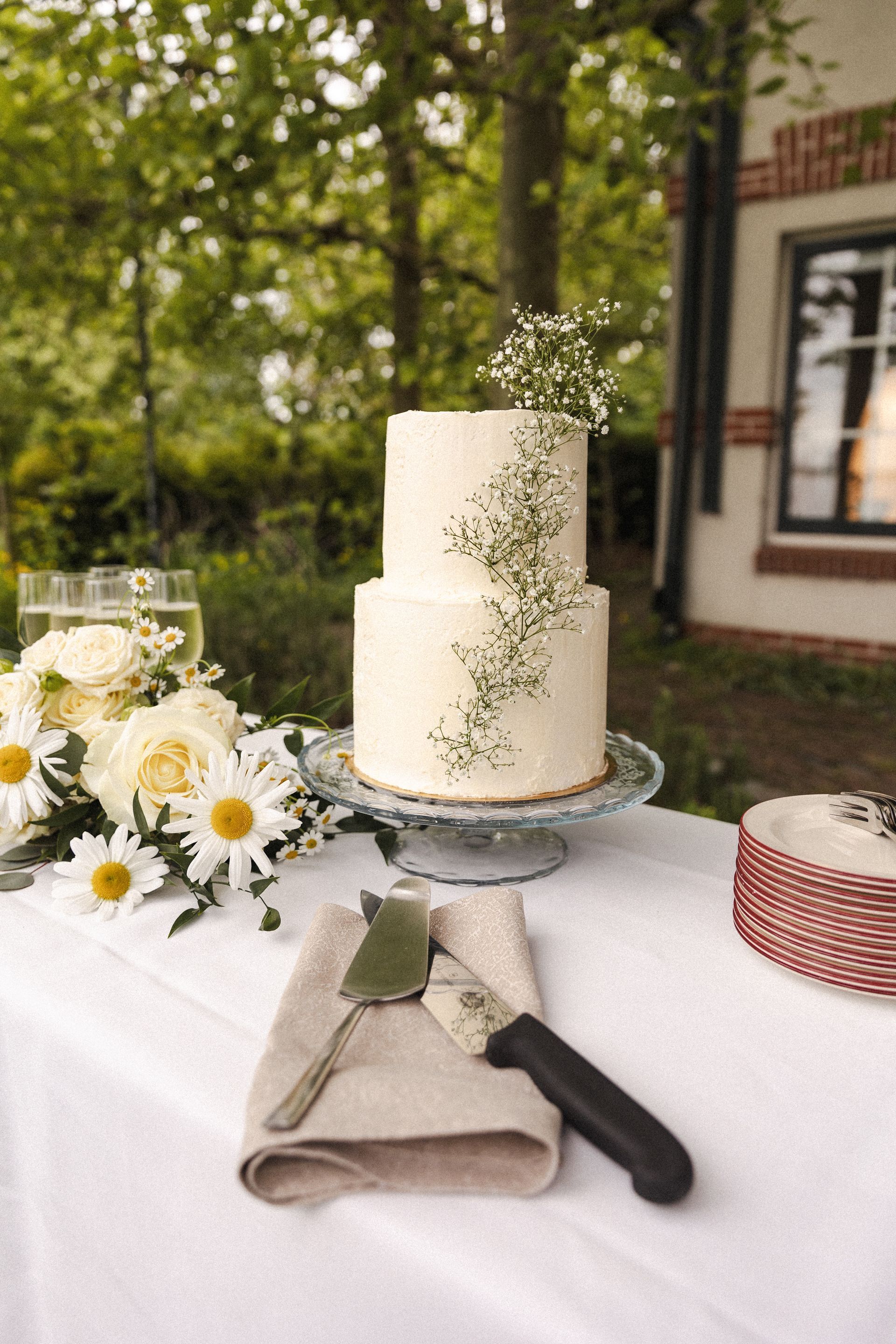 Minimalistische witte bruidstaart met subtiele bloemdecoratie, geplaatst in een groene en rustige buitenomgeving.