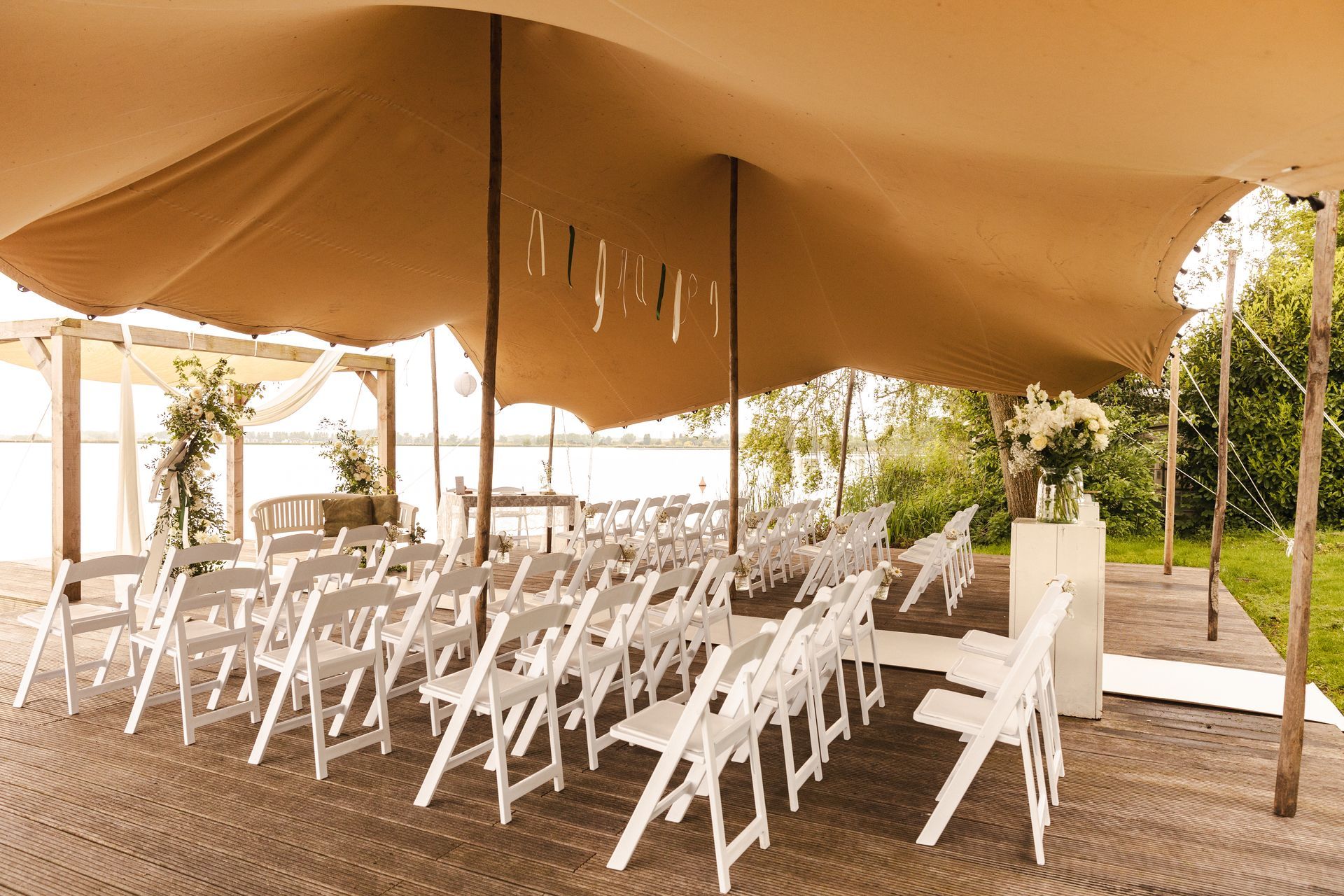 Buitenopstelling voor een huwelijksceremonie met witte stoelen onder een tent, klaar voor een sfeervolle en ontspannen bruiloft.