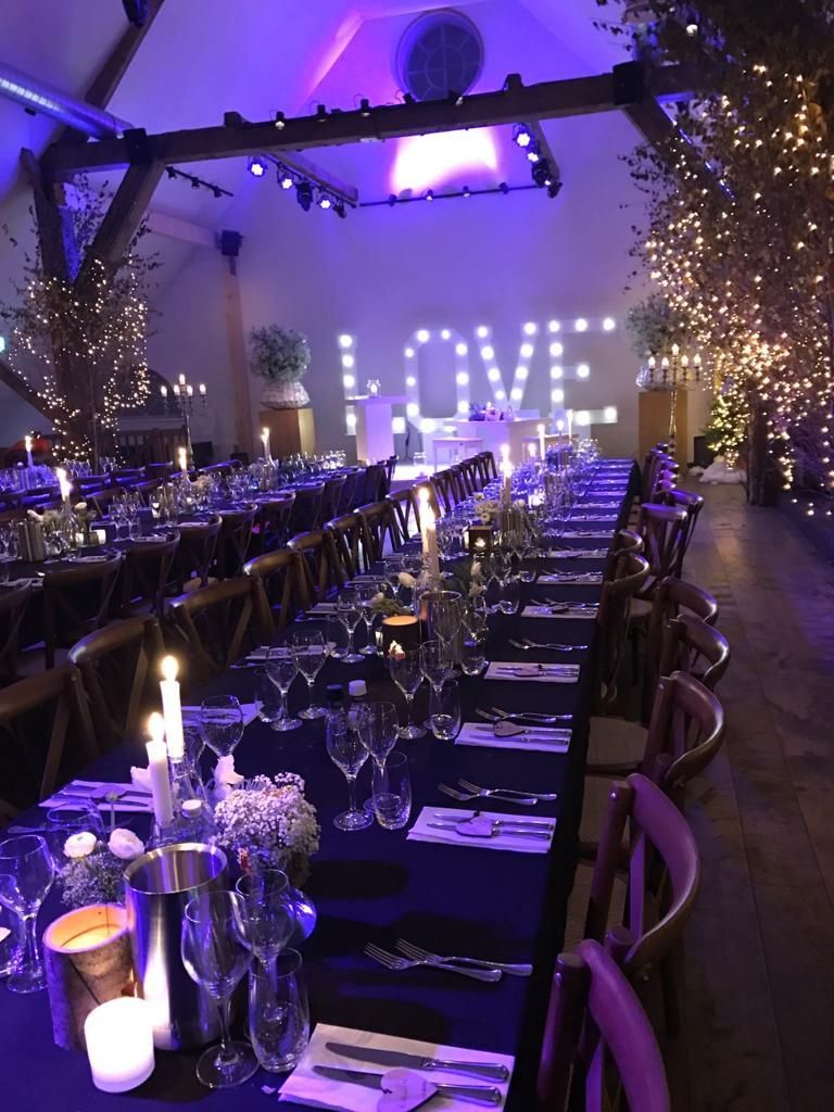 Sfeervol ingerichte trouwlocatie met lange dinertafels, kaarslicht en grote verlichte letters LOVE voor een romantische huwelijksviering.