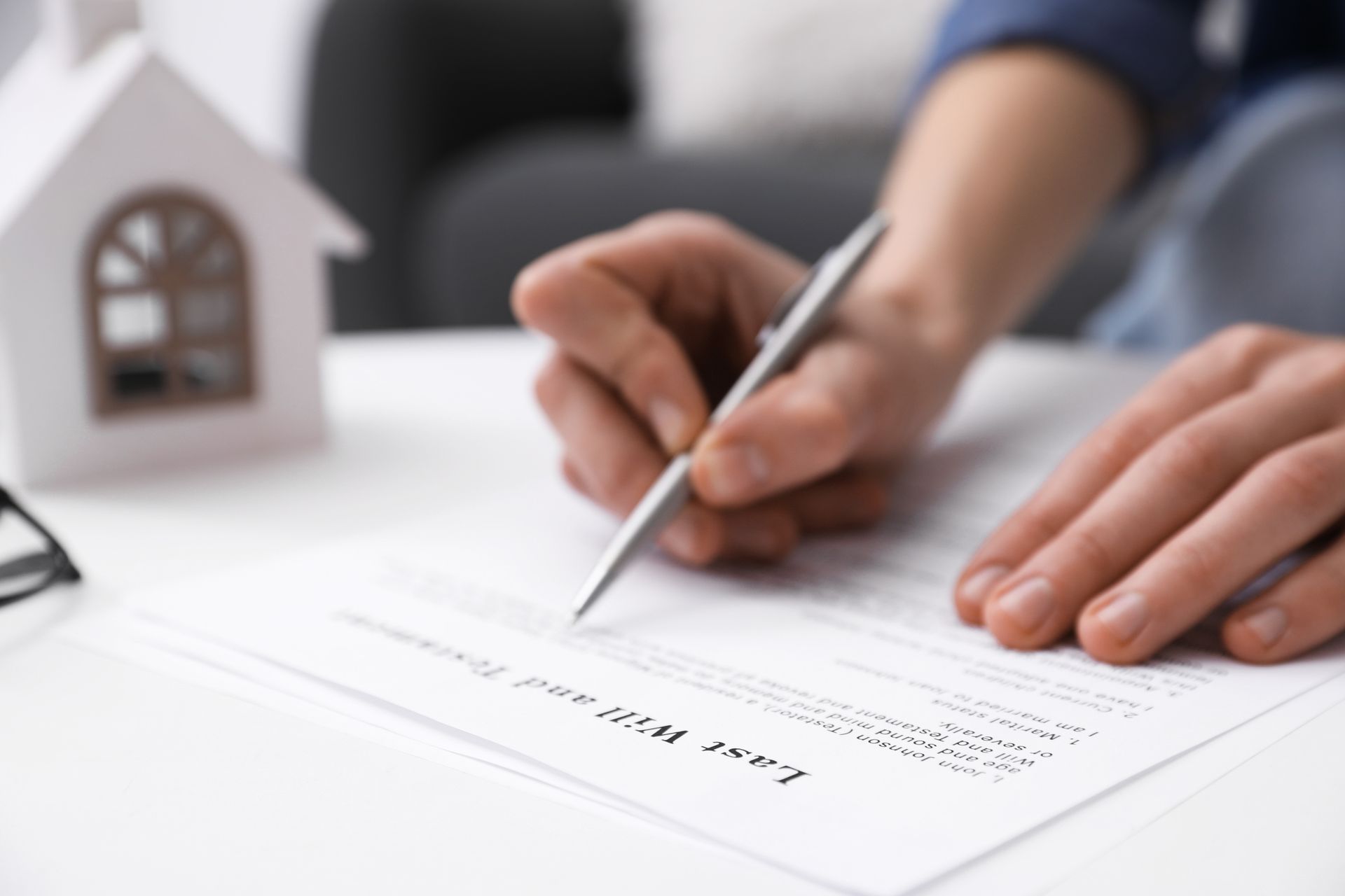 Close-up of hands signing a document beside a small house model on a desk.