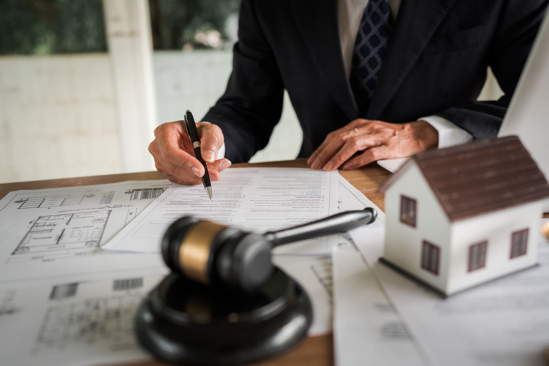 Lawyer signing documents beside house model and gavel on desk