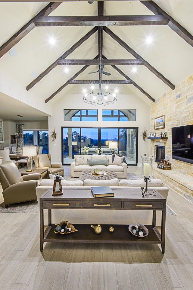 Spacious modern living room with exposed beams, stone fireplace, chandelier, and large windows