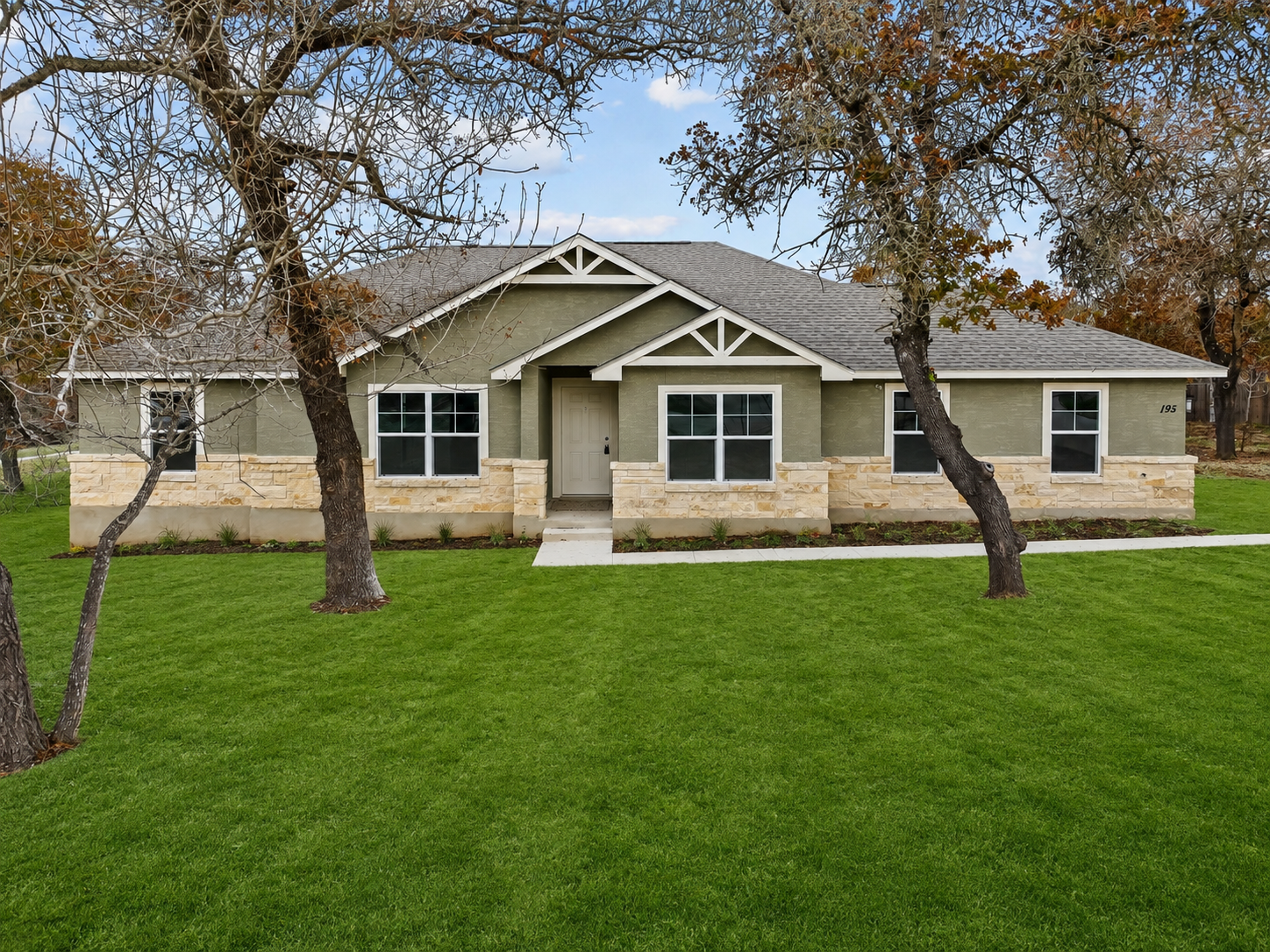 Single-story beige house with white trim, front porch, and large green lawn under trees.