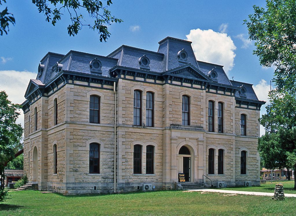 Stone historic mansion with a dark roof, tall windows, and a grassy lawn under a blue sky