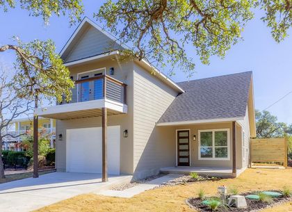 Modern two-story beige house with balcony, garage, and sloped roof on a sunny day