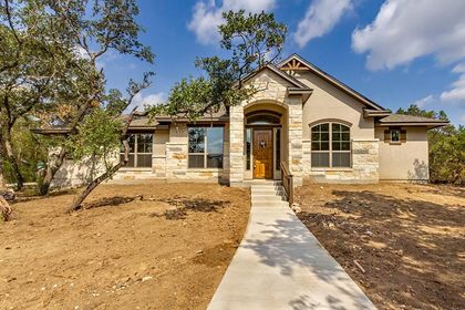 Stone single-story house with front walkway, arched entry, and dry yard under trees