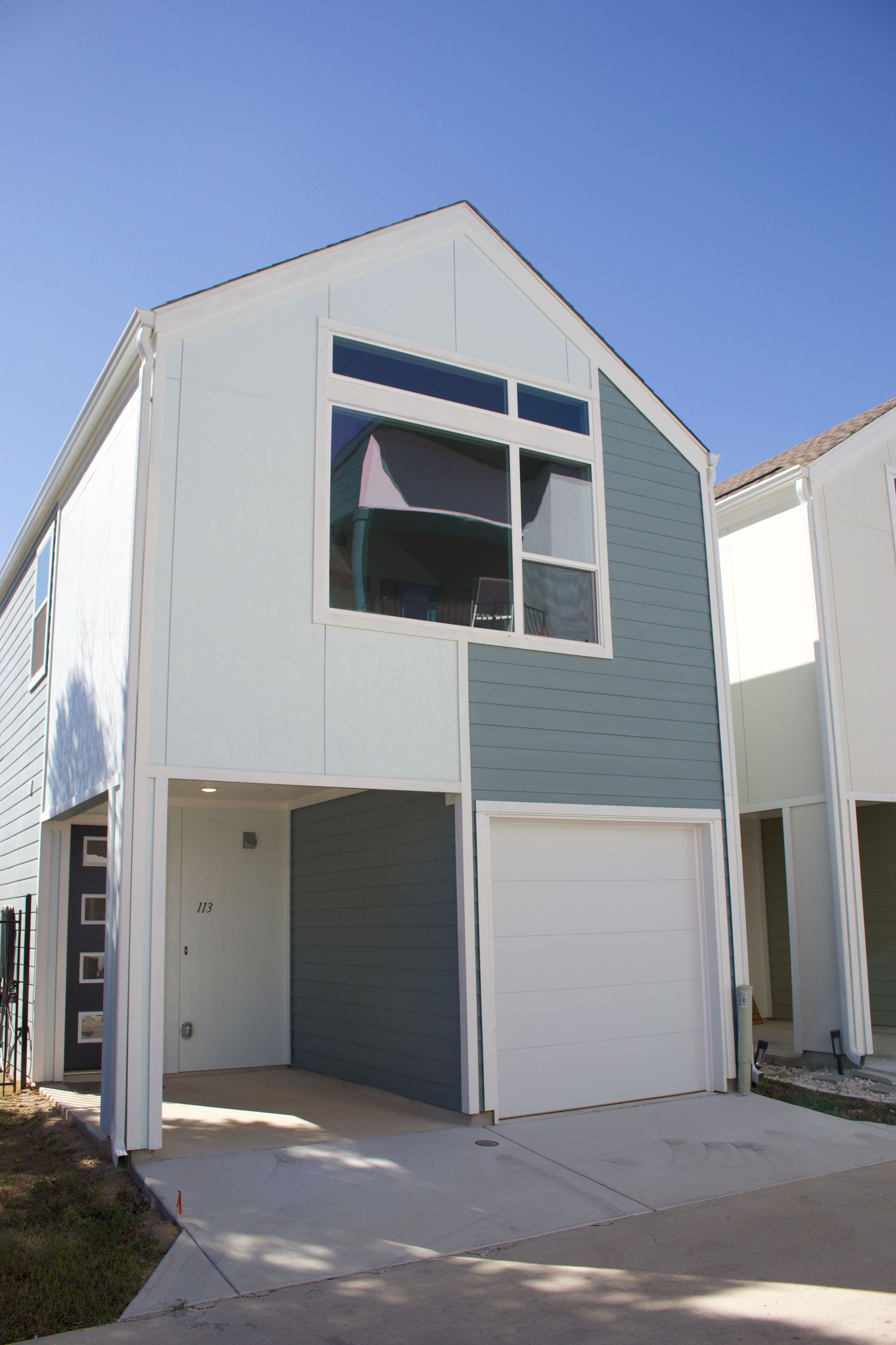 Modern two-story townhouse with white and light blue exterior, garage, and covered entry under a clear sky