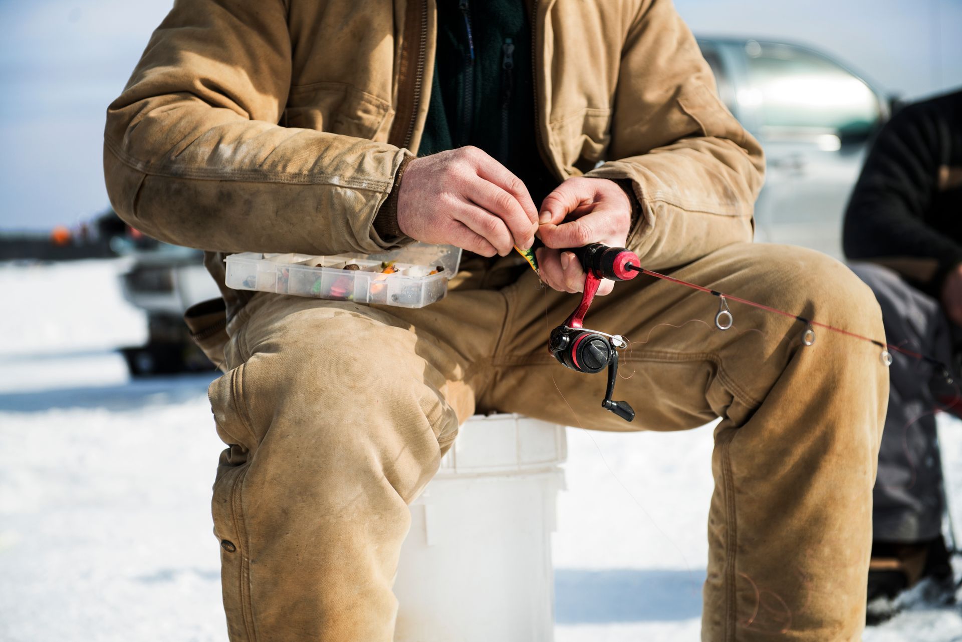 A man is sitting on a bucket in the snow fishing.